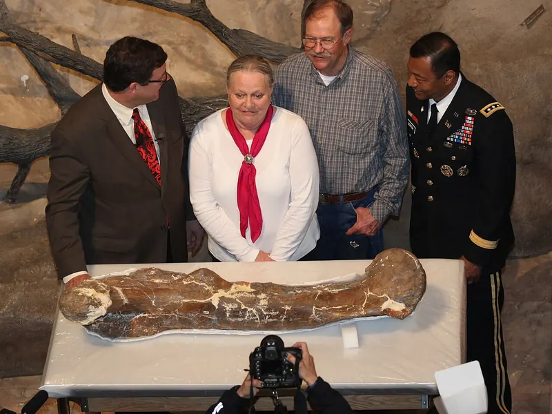 Four people standing behind a large fossil bone on a table at a press event